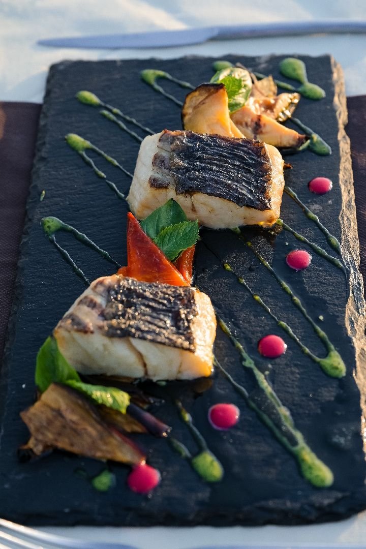 Piatto di pesce impiattato su ardesia con salse colorate