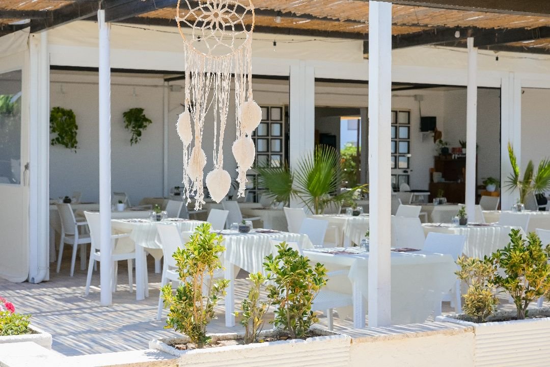 La sala all'aperto con i tavoli bianchi e le piante sotto la pergola